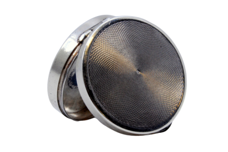 Caixa de comprimidos em prata guilhochada em forma circular e tampa basculante.